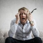 Stressed man sitting on couch, feeling overwhelmed and frustrated, expressing mental strain.
