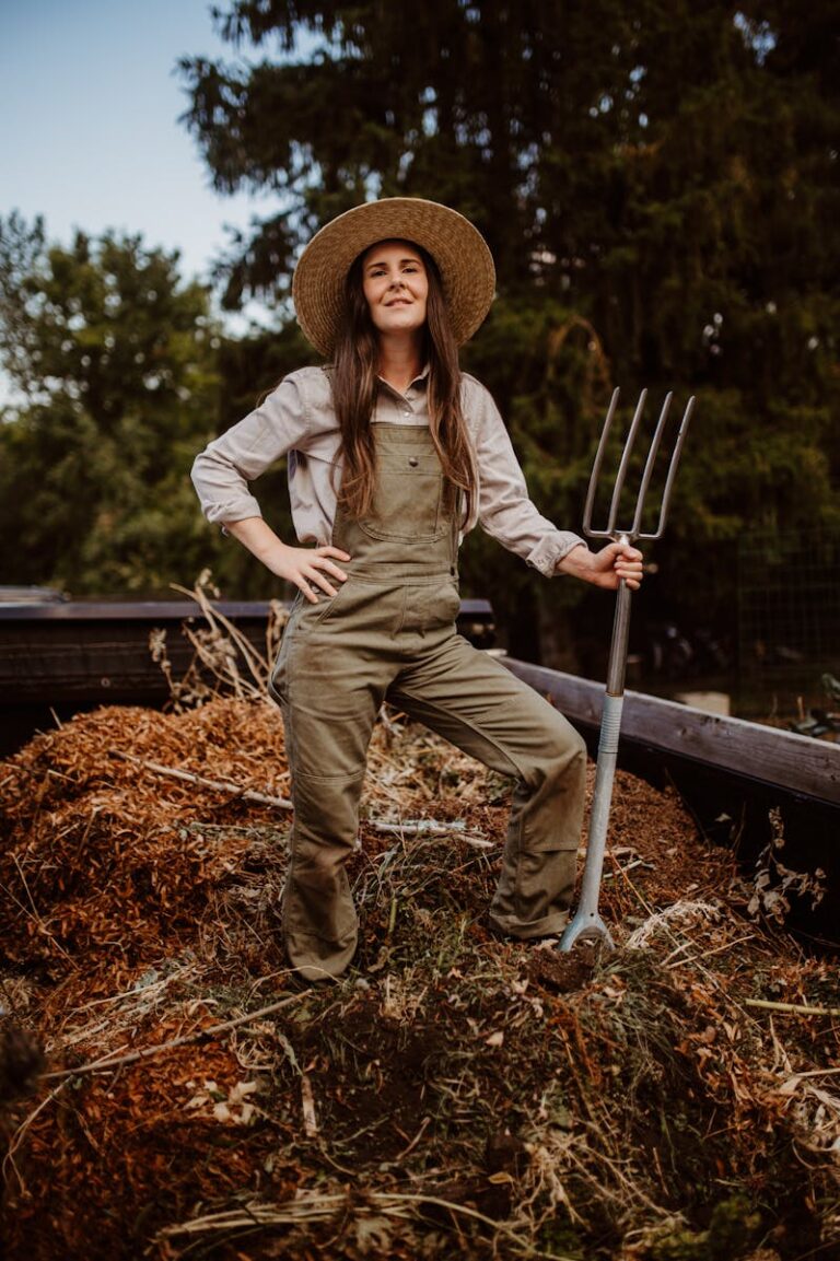 Woman gardener proudly standing with pitchfork by a compost heap outdoors.