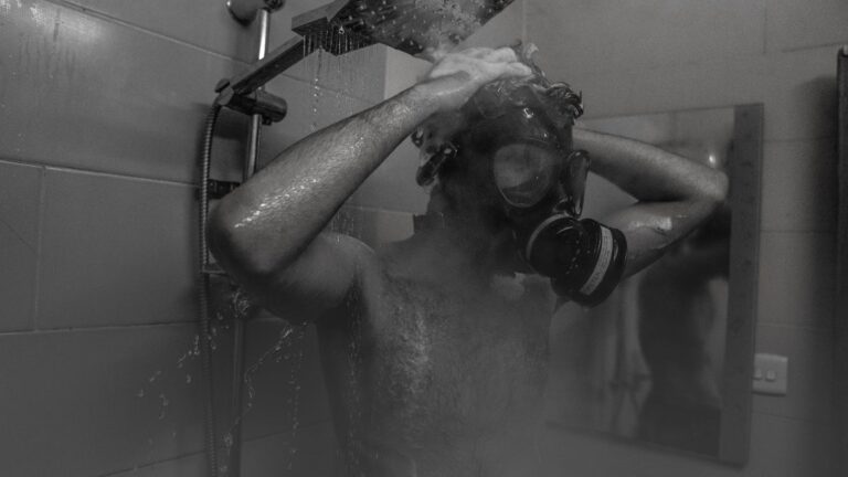 A man wearing a gas mask taking a shower in a monochrome setting.